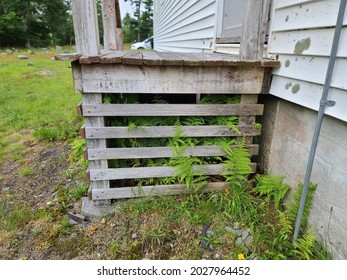 The Edge Of A Doorstep Where The Steps Have Fallen Off. There Is No Way Of Easily Getting Through The Front Door. The Siding Next To The Wooden Stoop Is Full Of Mold And Rot. This House Is Not Kept.