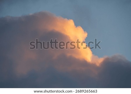 The edge of a dramatic dark cloud catches the warm golden light of sunset, creating a beautiful and hopeful background.