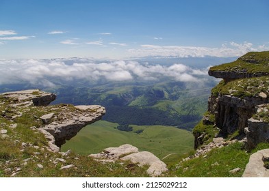 At the edge of rock formations. Beautiful view of the green valley and clouds from the Malyy Bermamyt Plateau. Nature and travel. Russia, Caucasus, Karachay-Cherkessia