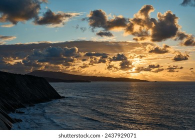 at the edge of steep and rugged cliffs of the gulf of biscay bay near St. Jean de Luz on the border between France and Spain with dramatic sunset and cloudscape.