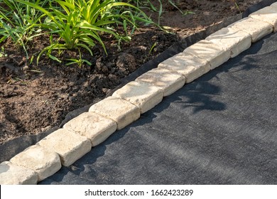 Edging of laid woven geotextile fabric with sandstone pavers in the summer garden under reconstruction - Shutterstock ID 1662423289