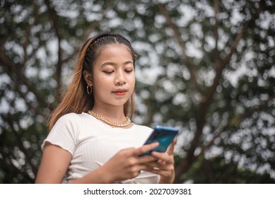 A Edgy Young Asian Woman Is Texting Or Chatting On Social Media While At The Park.