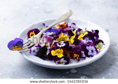 Edible flowers, field pansies, violets on white plate. Grey background. Close up.