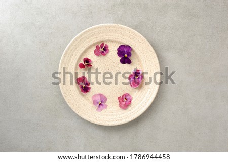 Edible flowers viola in the plate  on the gray background.  Healthy food background. Flat lay in horizontal orientation.