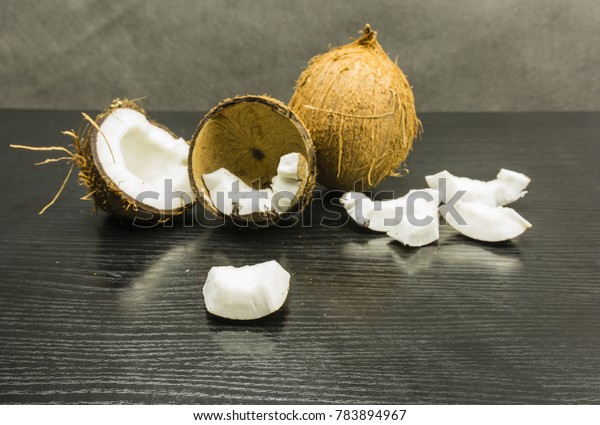 Edible part of a coconut on a wooden\
table. In the background, a whole and broken\
coconut.