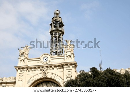 The Edificio de Correos y Telégrafos (Post and Telegraph Building) stands in Valencia, Spain. The structure features a large clock on the front and decorative statues on the roof. Clear blue skies are visible above the building.
