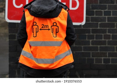 EDINBURGH, SCOTLAND - 05 February 2021 One Person Seen From Behind Wearing An Orange High Visibility Vest With A 2m Distancing Sign On The Back