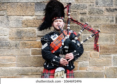 EDINBURGH, SCOTLAND, 24 March 2018 , Scottish bagpiper dressed in traditional red and black tartan dress stand before stone wall. Edinburgh, the most popular tourist city destination in Scotland.

