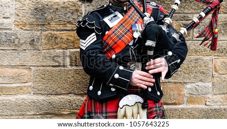 EDINBURGH, SCOTLAND, 24 March 2018 , Scottish bagpiper dressed in traditional red and black tartan dress stand before stone wall. Edinburgh, the most popular tourist city destination in Scotland.
