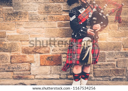 EDINBURGH, SCOTLAND, 24 March 2018 , Scottish bagpiper dressed in traditional red and black tartan dress stand before stone wall. Edinburgh, the most popular tourist city destination in Scotland.