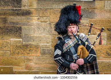 Edinburgh, Scotland - Dec 2018. Scottish bagpiper dressed in traditional red and black tartan dress playing bagpipe on the Royal Mile.