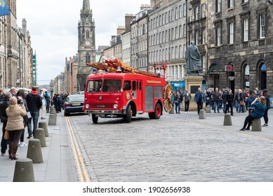 Edinburgh Scotland October 2019 Classic Old Red Silver Bedford Fire Engine Service With Wooden Extendable Ladder Driving On High Street Cobble Stones Shoppers Watching Church Sunny City Centre 