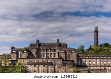 Edinburgh, Scotland, UK - June 13, 2012: Large Brown Building Was Old Royal High School And Abandoned Site Of New Scottish Assembly With Nelson Monument In Back, All Under Blue Cloudy Sky.