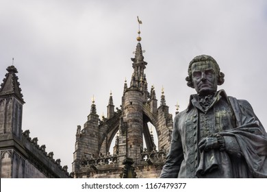 Edinburgh, Scotland, UK - June 14, 2012: Adam Smith Bronze Statue On Market Square In Front Of Brown Stone Saint Gilles Cathedral Crown Tower Under Gray Silver Sky. 