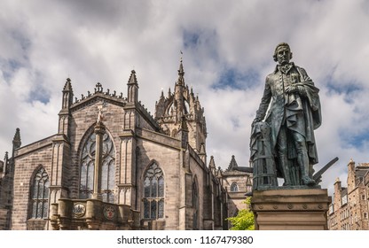 Edinburgh, Scotland, UK - June 14, 2012: Adam Smith Bronze Statue On Market Square In Front Of Brown Stone Saint Gilles Cathedral Crown Tower Under Gray Silver Sky With Blue Patches. Mercat Cross.