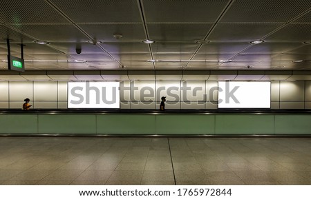 Edited visual for advertising billboard display: Pedestrians walking on moving walkway / travelator in train station. Blank billboards advertising space for mock up purpose; OOH ad placement.