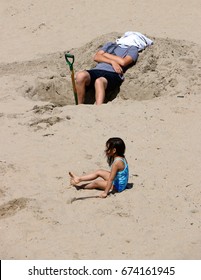 EDITORIAL.  Jul 2, 2017.  Capitola, CA.  Man At The Beach With Towel Around His Head After Digging A Hole; A Small Child Sits Nearby.