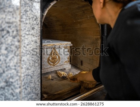 Editorial photo of a traditional cremation chamber in a Thai Buddhist temple, featuring a decorated coffin and ceremonial flower offerings. 