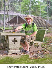 Editorial Use Only; A Man In A Green Tee Shirt, And Straw Hat Sitting At A Stone Table Outdoors, Taken At Sisaket, Thailand, In June 2022.   