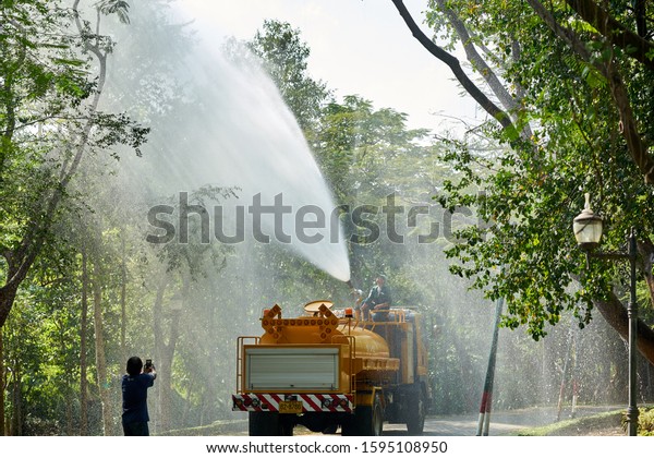 Editorial use only; a truck sprays water green\
trees and plants in sunlight, in a park in Bangkok, Thailand, in\
December 2019.