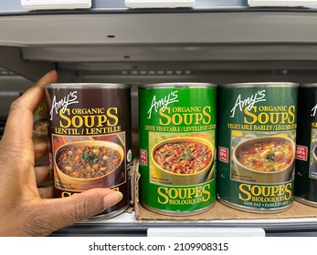 Edmonton, Canada - January 4, 2022: Black Person Reaching For Cans Of Amy's Kitchen Soup, Made In California, On A Grocery Store Shelf