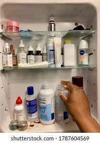 Edmonton, Canada - July 10, 2020: A Black Person Reaching For Contact Lens Solution In A Medicine Cabinet With Various Skincare Products And Toiletries