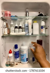 Edmonton, Canada - July 10, 2020: A Black Person Reaching For Contact Lens Solution In A Medicine Cabinet With Various Skincare Products And Toiletries