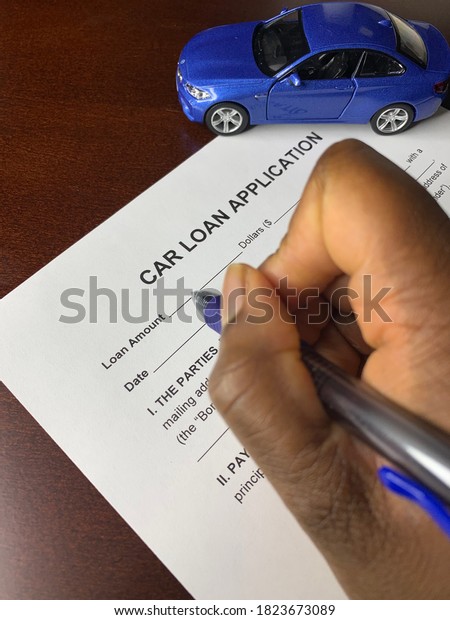 Edmonton, Canada - September 24, 2020:\
A closeup concept picture of a Black person’s hand signing a car\
loan application with a blue model car in the background\
