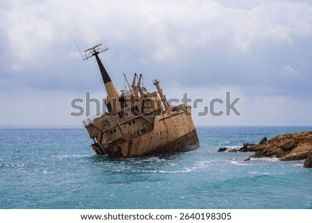 The Edro III shipwreck rests tilted near the rocky coast of Cyprus, surrounded by calm turquoise waters under a partly cloudy sky.