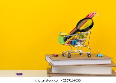 Education, Back To School. Shopping Cart With Supplies Near Pile Of Books.Defocused Image