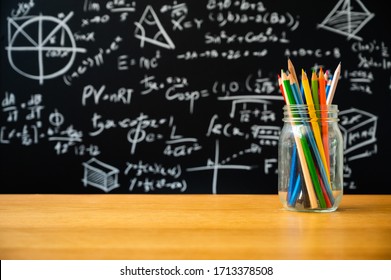 Education Background Concept. Stationery In Glass Jar Color Pencil, Compasses Tool, Scissors, Rulers, Sharpener On Chalkboard With The Mathematical Formula Background.