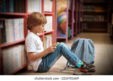 Education. A boy in casual clothes sits on the floor in the library reading a book. Modern children.  - Powered by Shutterstock
