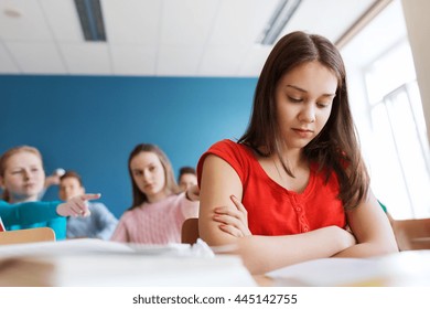 Education, Bullying, Conflict, Social Relations And People Concept - Students Teasing And Judging Girl Classmate Behind Her Back At School