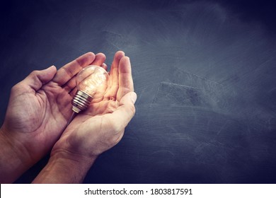 Education and business concept image. Creative idea and innovation. Man holding a light bulbs as metaphor over blackboard background