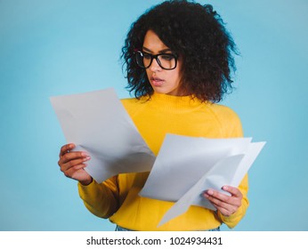 Education And Business Concept - International Student Studying In College. Or Modern African American Businesswoman With Afro Hairstyle Reading Documents On Blue Background In Studio.