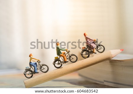 Education and Business concept. Miniature people : Small figures cycling on red color pencil using as background.