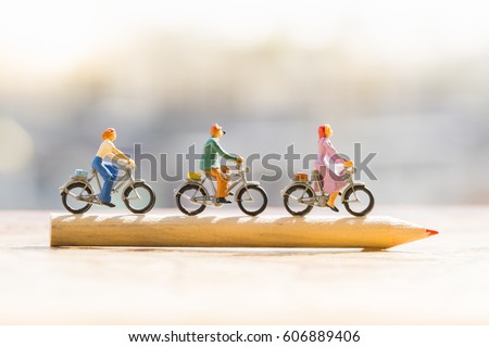 Education and Business concept. Miniature people : Small figures cycling on red color pencil using as background.