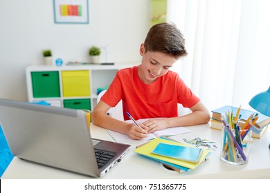 education, childhood and people concept - happy student boy with laptop computer writing to notebook at home