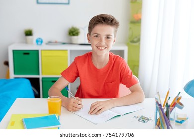 Education, Childhood And People Concept - Happy Student Boy Writing To Notebook At Home