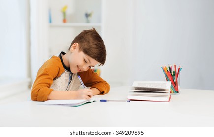 Education, Childhood, People, Homework And School Concept - Smiling Student Boy With Book Writing To Notebook At Home