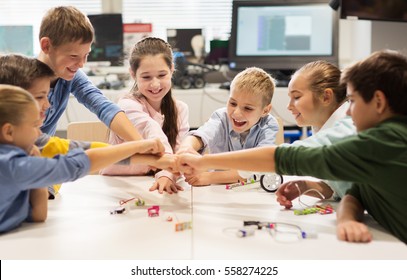 Education, Children, Technology, Science And People Concept - Group Of Happy Kids Building Robots At Robotics Lesson And Making Fist Bump