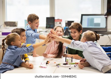 education, children, technology, science and people concept - group of happy kids building robots and making high five gesture at robotics school