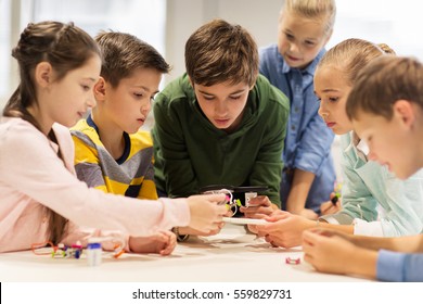 education, children, technology, science and people concept - group of happy kids building robots at robotics school lesson