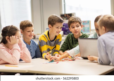 education, children, technology, science and people concept - group of happy kids with laptop computer building robots at robotics school lesson