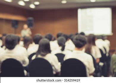 Education Classroom Blur Background Of University Students Sitting In A Lecture Hall Or Seminar Room With Teacher And White Projector Slide Screen In Front Of Class For Back To School Concept 