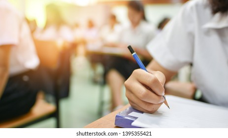 Education classroom concept image of student writing article or taking notes in the lecture room while participating in the training session of academic development; learner holding pencil taking exam - Shutterstock ID 1395355421