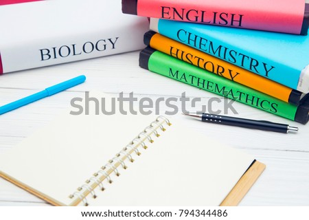 Education concept: school books on different subjects in bright covers and an opened notebook on a white wooden table, space for a text or product display