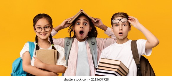 Education Concept. Set portrait of diverse schoolchildren posing looking at camera, holding stack of academic books and wearing backpack, yellow orange color studio background, panorama banner - Powered by Shutterstock