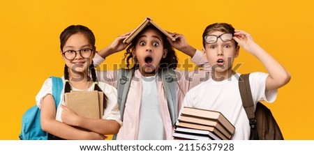 Education Concept. Set portrait of diverse schoolchildren posing looking at camera, holding stack of academic books and wearing backpack, yellow orange color studio background, panorama banner