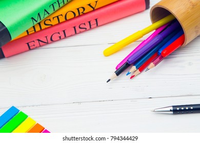 Education concept. Studying for exams. A stack os student's books and a pencilcase with colored pencils and markers on a white wooden table, space for a text or product display